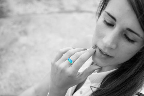 A black and white photo of a young woman. Shown in color, a blue opal ring with a gold band is worn on her finger.