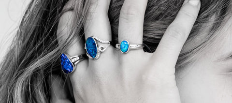 A woman wearing a range of white gold opal rings on her hand which is held up against her hair